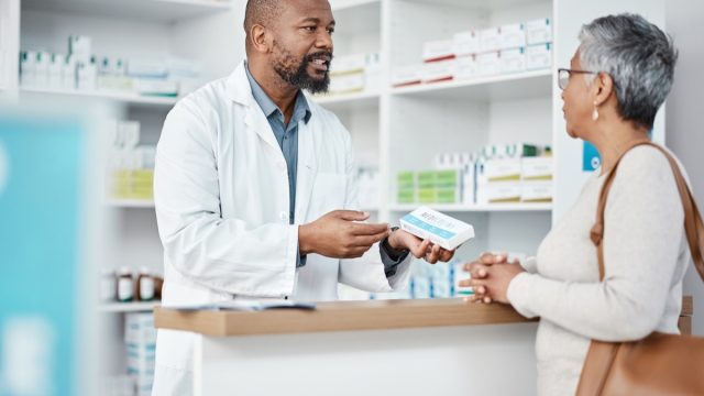 Healthcare, pharmacist and woman at counter with medicine or prescription drugs in hands at drug store. Health, wellness and medical insurance, man and customer at pharmacy for advice and pills.