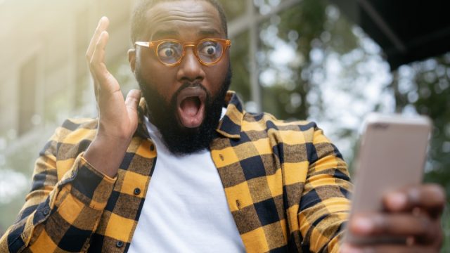 young man looking at his phone with his mouth open learning about emoji meanings