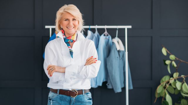 Fashionable mature woman standing in front of a rack of clothing wearing jeans and a white shirt