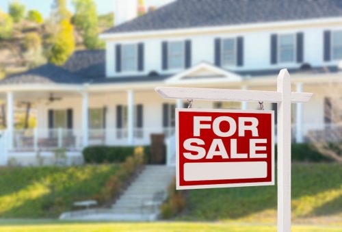 A for-sale sign in the foreground with a big white house in the background