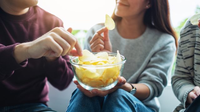 Closeup image of friends sharing and eating potato chips