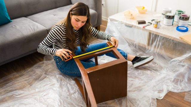woman measuring a chair while working on a furniture flipping project at home