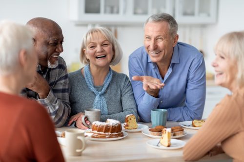 Three women and two men sitting around a table, laughing and eating cake