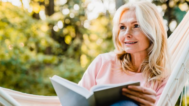 Beautiful,Senior,Blonde,Woman,Reading,Book,And,Sitting,In,Hammock