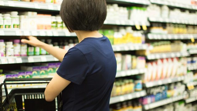 Woman Shopping at Grocery Market Pharmacy. Supermarket Shopper Doing Groceries. Female Holding Basket Trying to Decide which Products to Buy. Retail Healthcare Medicine, Vitamins, and Supplements.