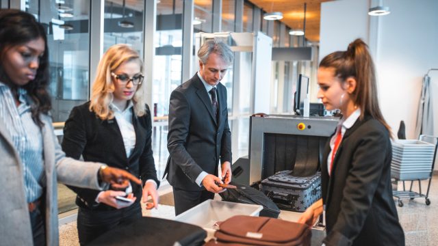 Travelers placing their items and luggage through an airport security checkpoint x-ray machine