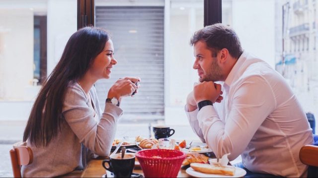 Woman and man sitting across from each other and drinking coffee at a cafe