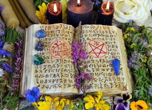 Witch book with spells and magic symbols, black candles, crystals and flowers