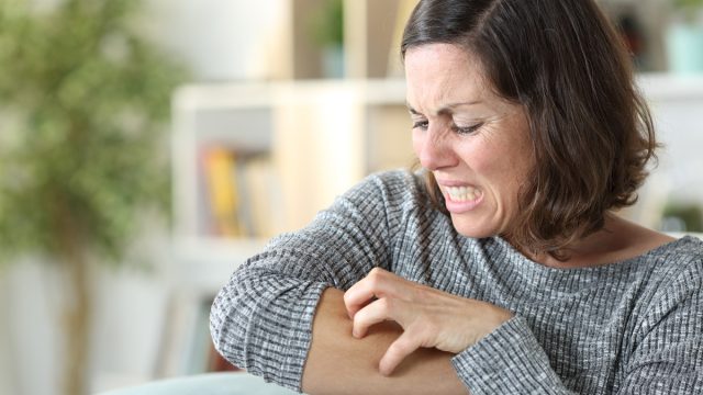 Middle age woman scratching itchy skin at home
