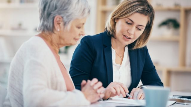 Talking finance worker helping senior with paperwork, budgeting and managing pension fund at home. Financial advisor explaining and showing old woman where to sign will agreement and banking contract