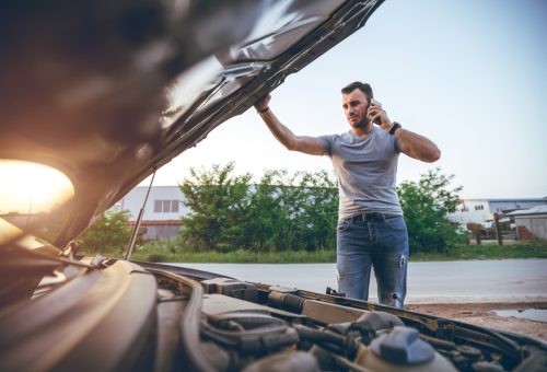 Young man calling roadside assistance after car breakdown