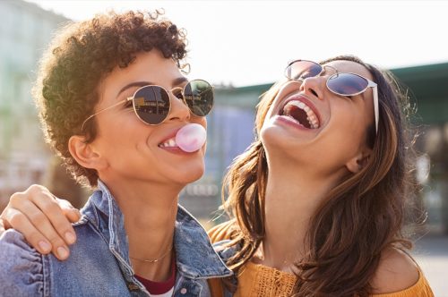 two female friends laughing and blowing bubbles with their gum