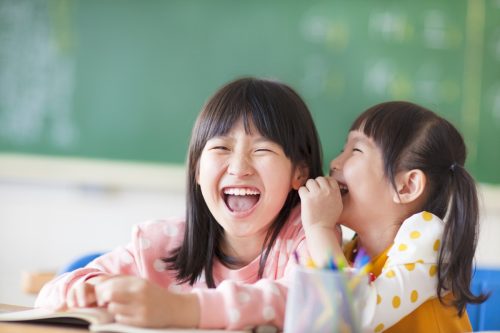 two little girls at school whispering to one another
