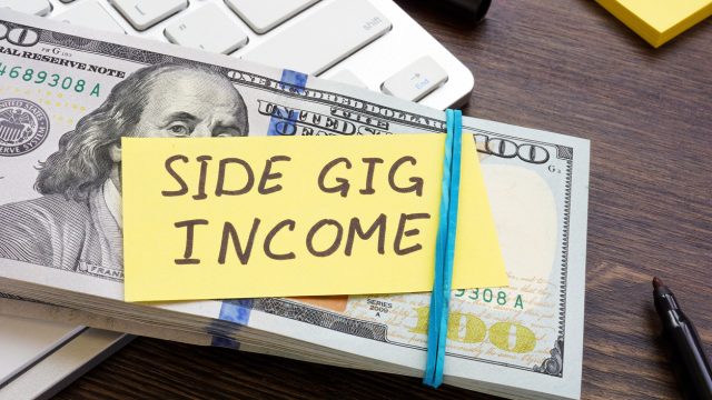 A stack of $100 bills with a note saying "side gig income" on top