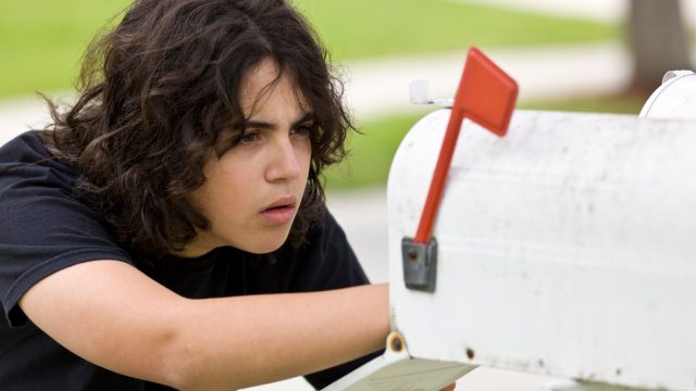 A young person looking into a white mailbox potentially stealing letters or packages