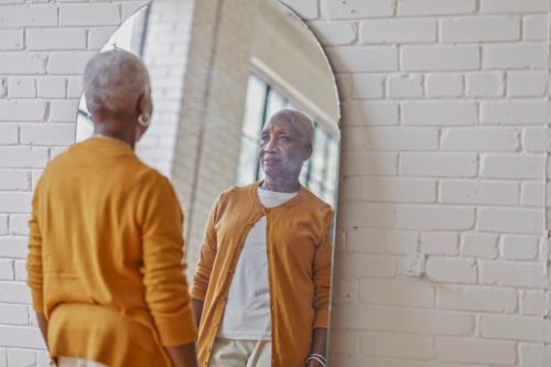woman looks at herself in the mirror. She is shopping for clothing and is deciding if she likes the outfit she has tried on.