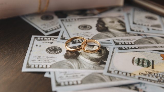 Two gold wedding bands sitting on top of a pile of hundred dollar bills.