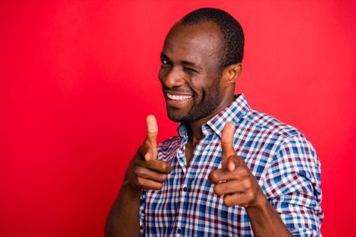 man winking and pointing at camera over a red backdrop