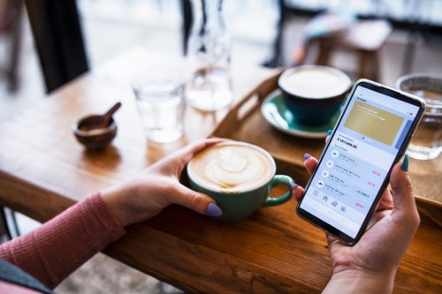 Young woman checking banking account via mobile app on smartphone while drinking coffee at Cafe.