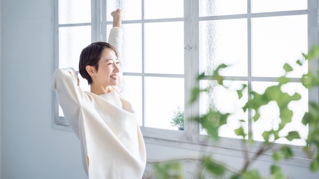 A woman dressed in white stretching and smiling in front of a large window