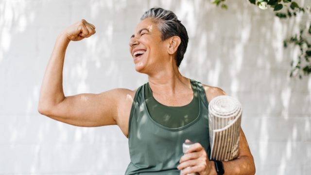 Happy older woman celebrating her fitness achievement after a great outdoor workout session, flaunting her strong bicep. Fit senior woman expressing her pride in her successful exercise routine.