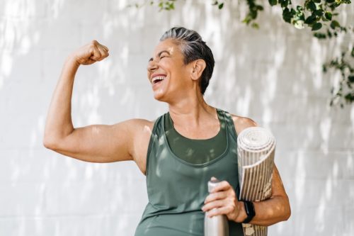 Happy older woman celebrating her fitness achievement after a great outdoor workout session, flaunting her strong bicep. Fit senior woman expressing her pride in her successful exercise routine.