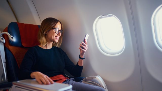 Traveling and technology. Flying at first class. Pretty young businees woman using smartphone while sitting in airplane.