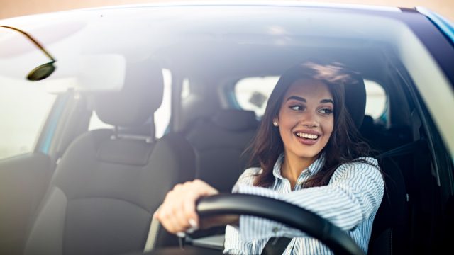Happy woman driving a car and smiling. Cute young success happy brunette woman is driving a car. Portrait of happy female driver steering car with safety belt