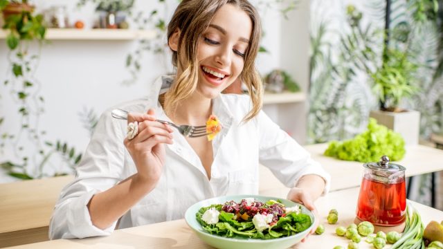 Young woman eating healthy food sitting in the beautiful interior with green flowers on the background