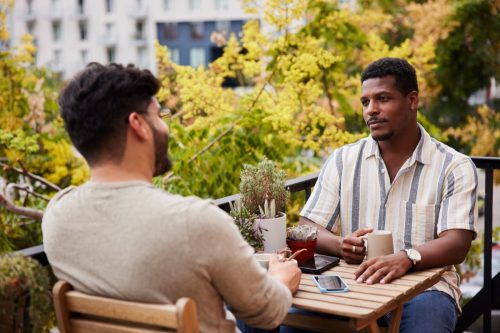 friends sitting on their apartment balcony in the city and talking over cups of coffee