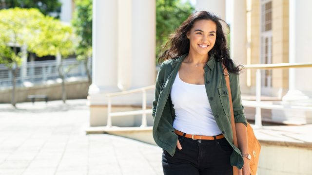 A smiling young woman wearing a casual outfit walks outside.