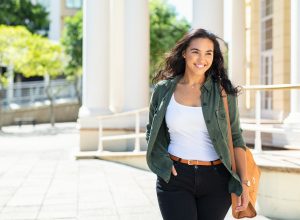 A smiling young woman wearing a casual outfit walks outside.