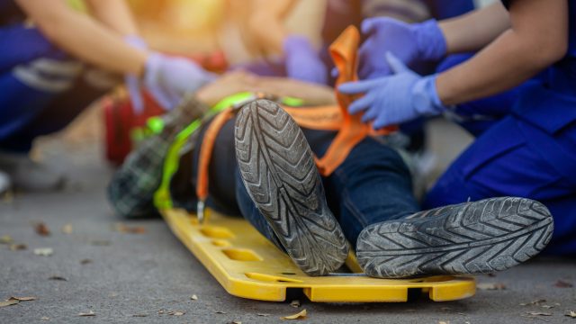 A close up of an injured person's feet lying on a road as they're loaded onto a a stretcher board by EMTs