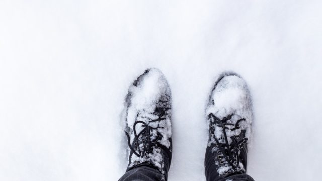 feet in black boots on snowy ground. The arrival of winter and snowy weather.