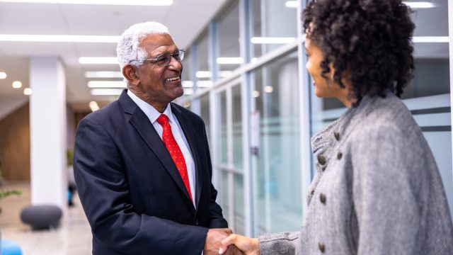 Senior Black businessman and young woman meeting sharking hands in the hallway
