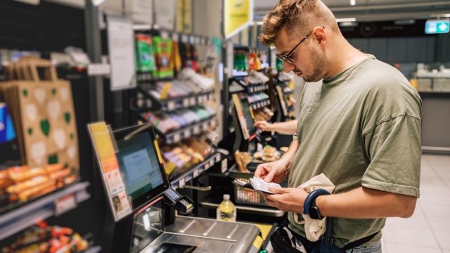 Man buying and paying money in the supermarket. Photo with people in the store during the shopping. Person is using contactless payment