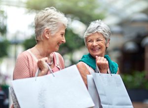 Two senior female friends holding shopping bags and smiling at each other.