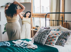 Curly haired curvy woman looking in bedroom mirror