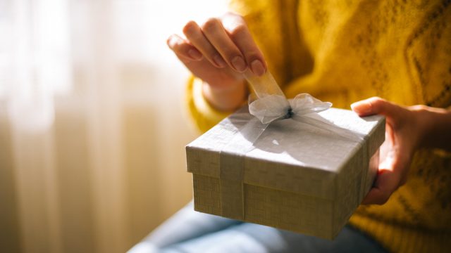 Young woman in yellow sweater opening gift box