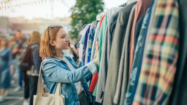 A young woman looking through a vintage clothing rack at a sale or market