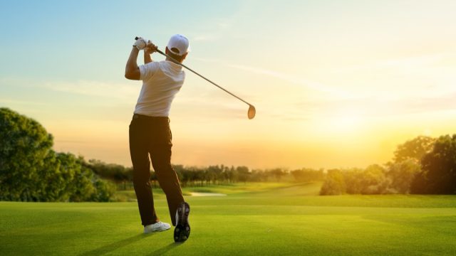 Golfer hit sweeping driver after hitting golf ball down the fairway with sunrise background.
