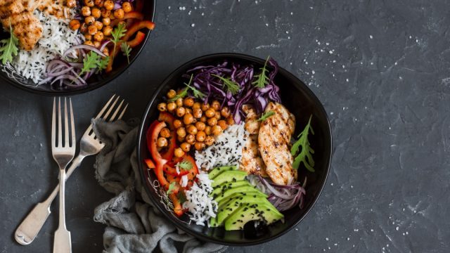 Grilled chicken, rice, spicy chickpeas, avocado, cabbage, pepper buddha bowl on dark background, top view. Delicious balanced food concept