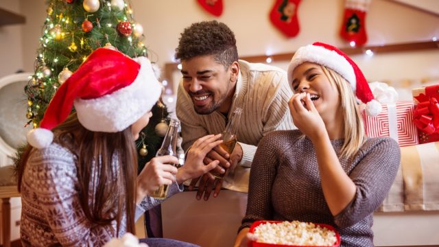 group of friends eating popcorn in front of the tree telling christmas jokes