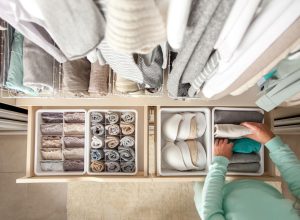 Unidentified neat housewife puts container with socks and pantyhose on wardrobe drawer during general cleaning by modern storage system. Concept of beautiful and comfortable organization
