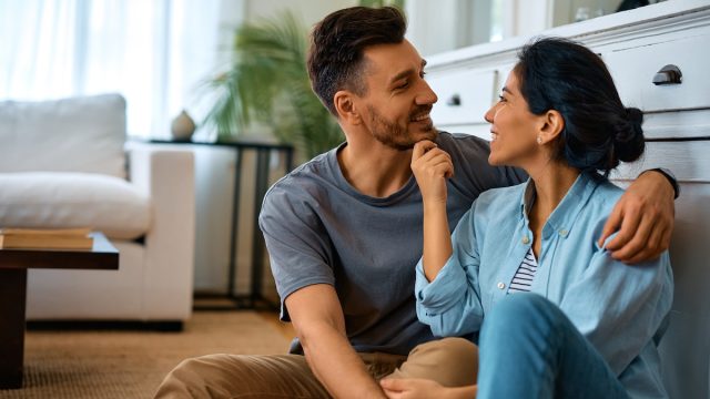 A happy couple sitting on the living room floor and talking.