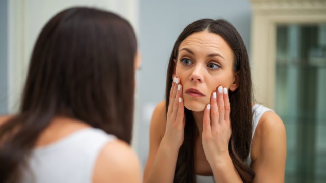 Tired woman looking at her eye bags in the bathroom.