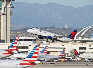 A Delta plane taking off from an airport with American Airlines planes visible in the foreground