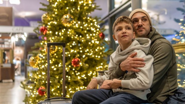 A father and son sitting next to a Christmas tree in an airport terminal waiting for a flight