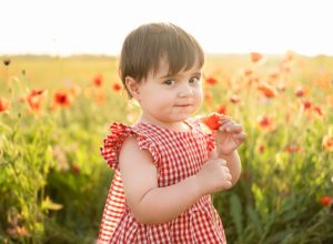 little girl in a red dress holding a flower in front of a field of poppies