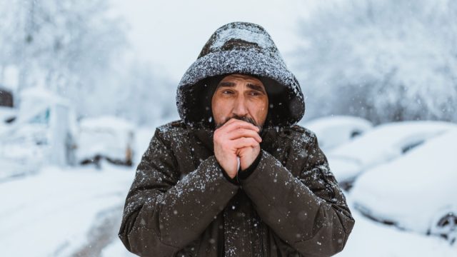 Portrait shot of the caucasian good looking mature  man in casual style is freezing on the cold winter day while standing in the center city.